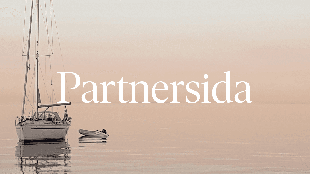 A small sailboat anchored at sea. The water is still like a mirror, and blends seamlessly with the pink evening sky.