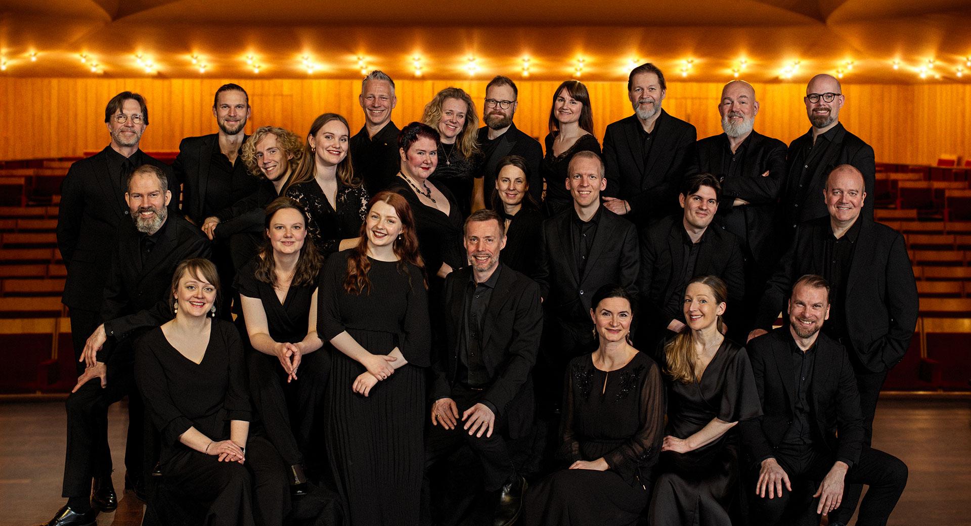 Bild på Radiokören klädda i svart, framför en upplyst vägg