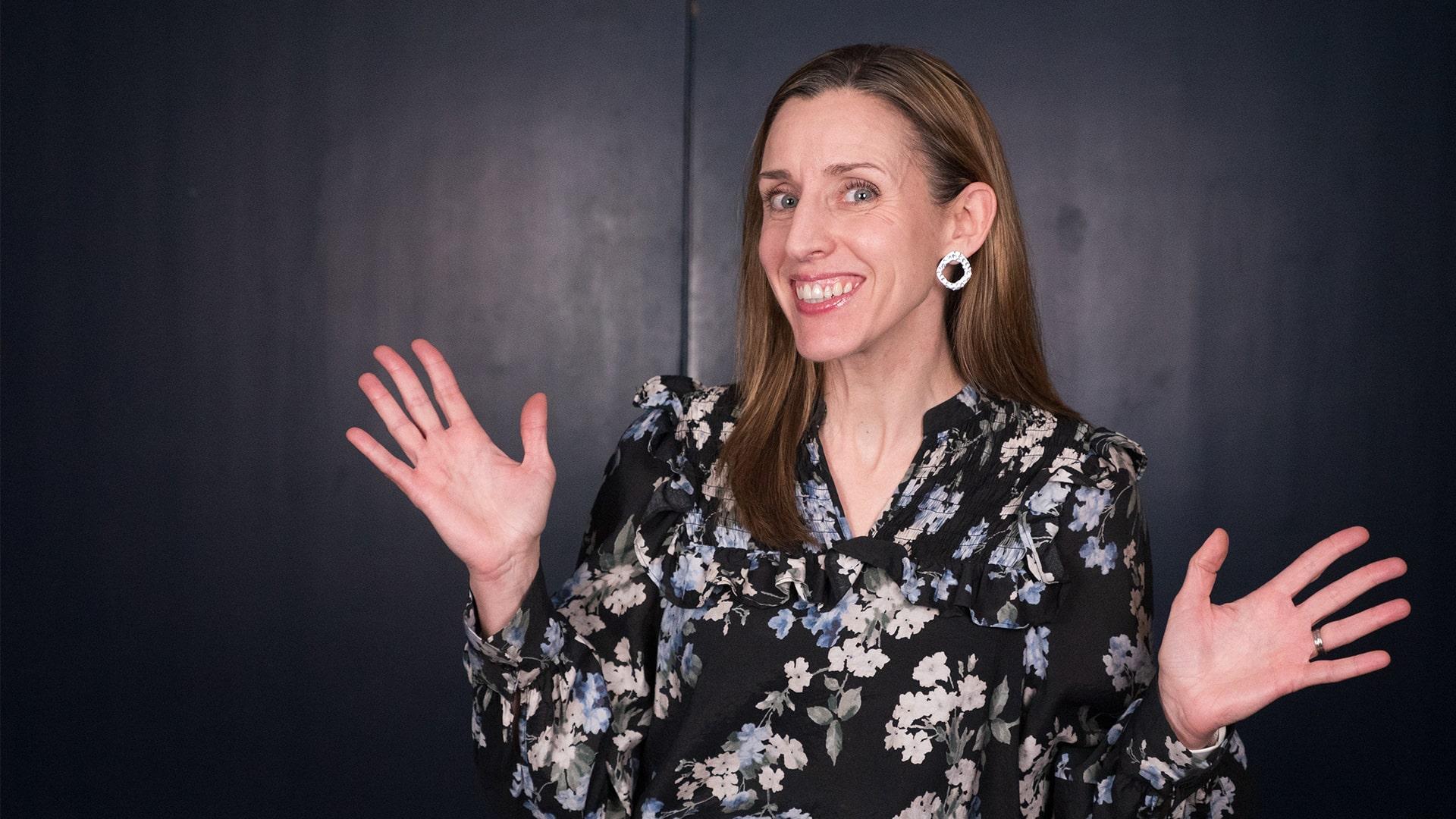 Anna Graca, Radiokören. Kvinna som ler stort och slår ut med händerna i en positiv gest. Hon har långt hår, runda silverringar i öronen och en blommönstrad blus i svart, grått och ljust blått.