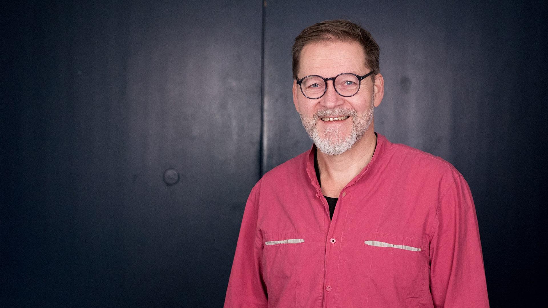 Johan Pejler, Radiokören. Närbild på leende man med glasögon och kort skägg. Han tittar in i kameran och är klädd i en färgglad skjorta.