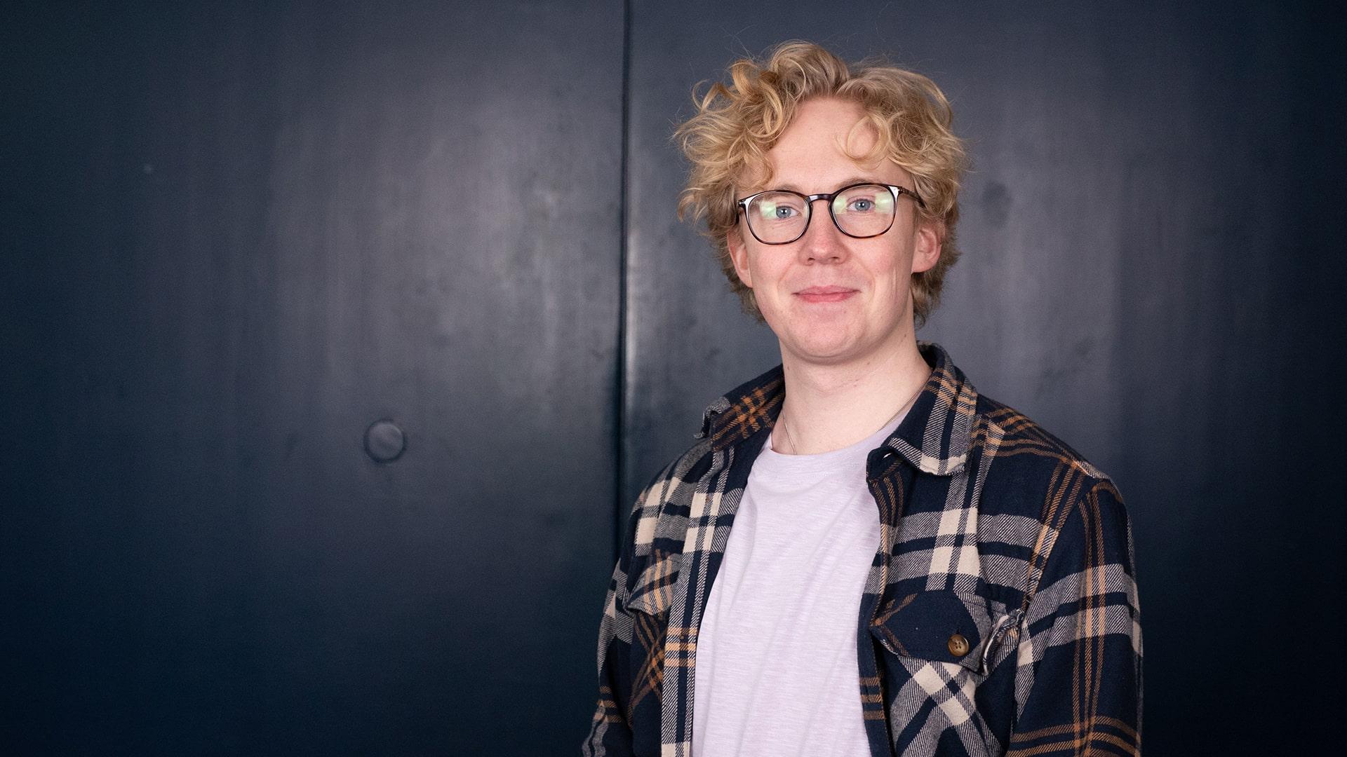 Jonas Törnqvist, Radiokören. Bild på leende man med lockigt ljust hår och mörka glasögonbågar. Han tittar in i kameran och är klädd i rutig uppknäppt skjorta med en ljust lila t-shirt under.