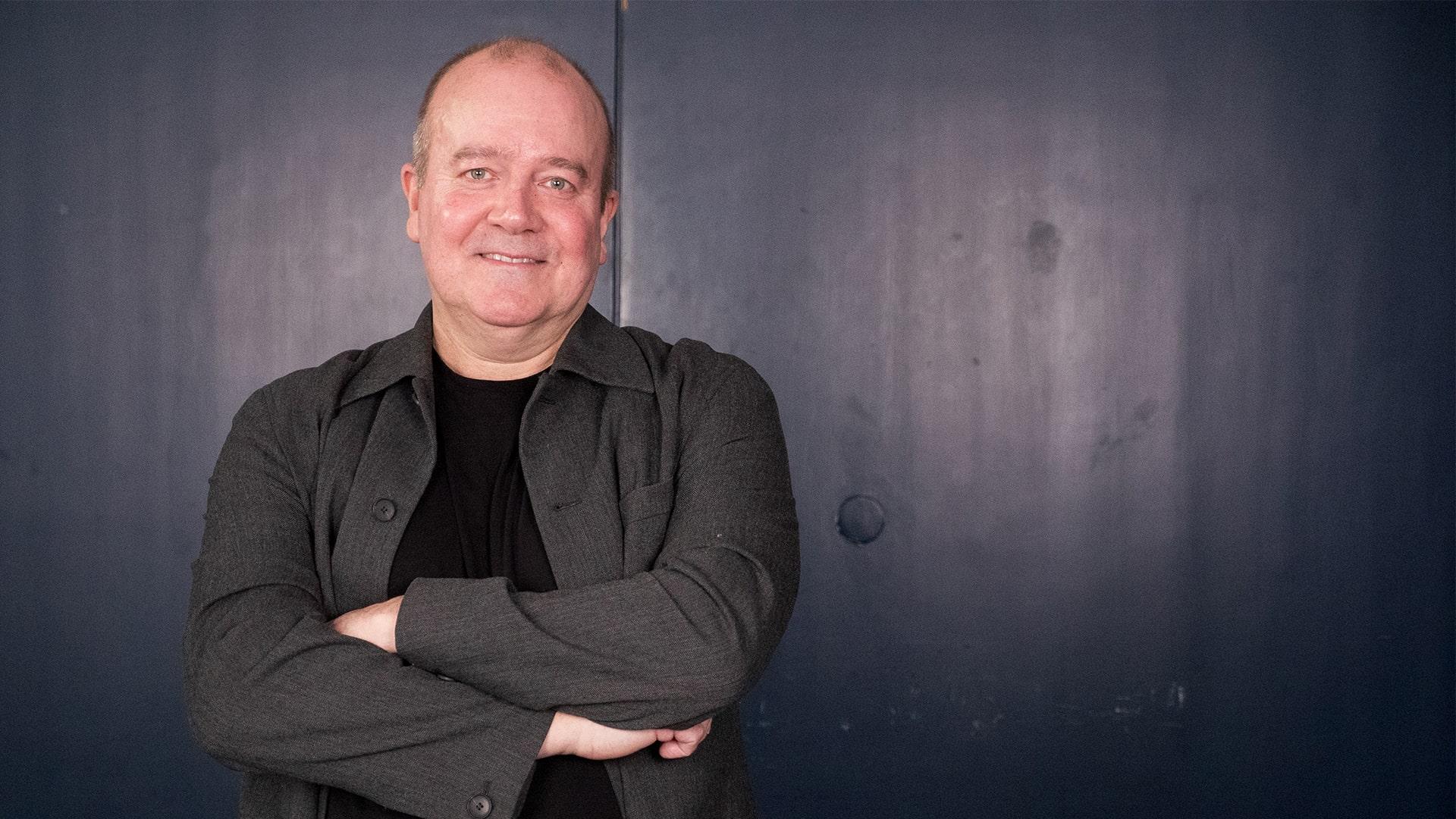 Mats Carlsson, Radiokören. Närbild på leende man med armarna i kors över bröstet, klädd i grå skjorta