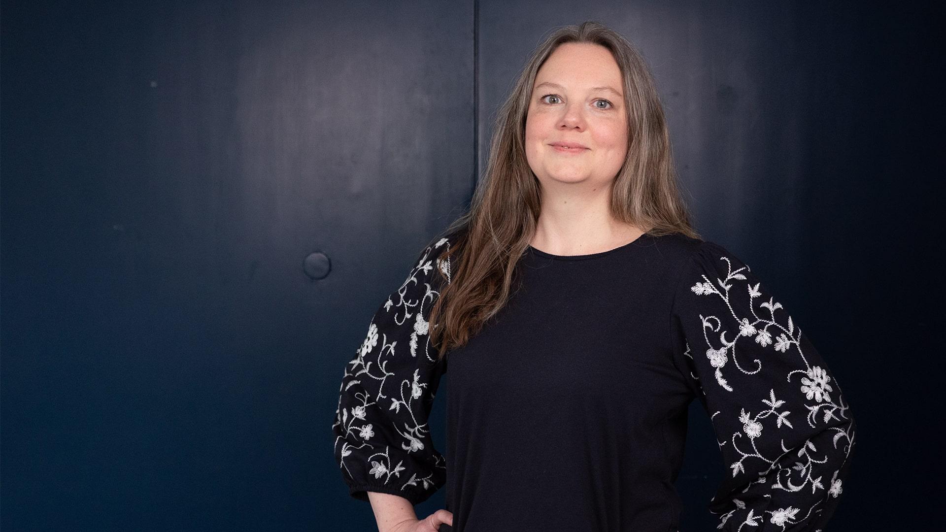 Ingrid Radholm Konvicka, Radiokören. Kvinna med långt utslaget hår tittar rakt i i kameran. Hon har händerna i sidorna och är klädd i svart med ett rankande blommönster i vit brodyr.