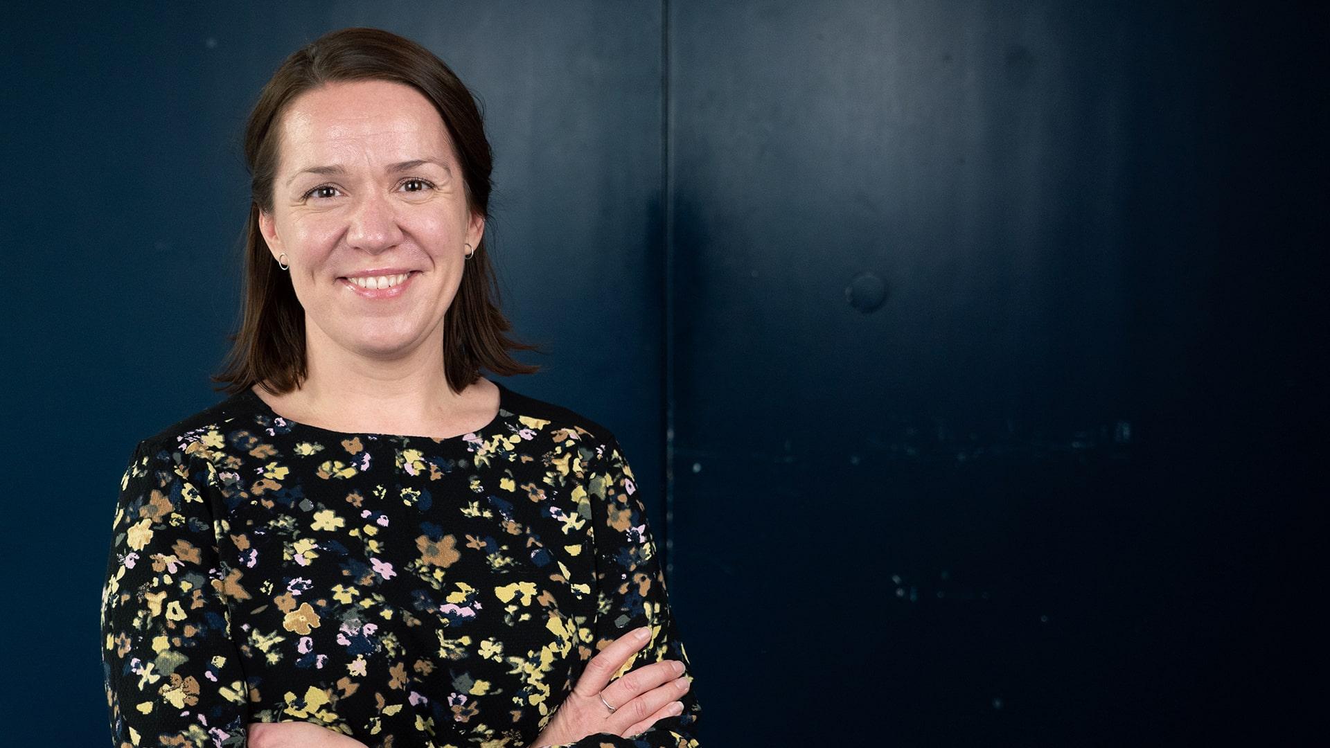 Jaanika Kuusik, Radiokören. Leende kvinna tittar rakt in i kameran. Hon har mörkt hår i pagefrisyr och är klädd i en blommig blus i gult och rosa på svart botten.