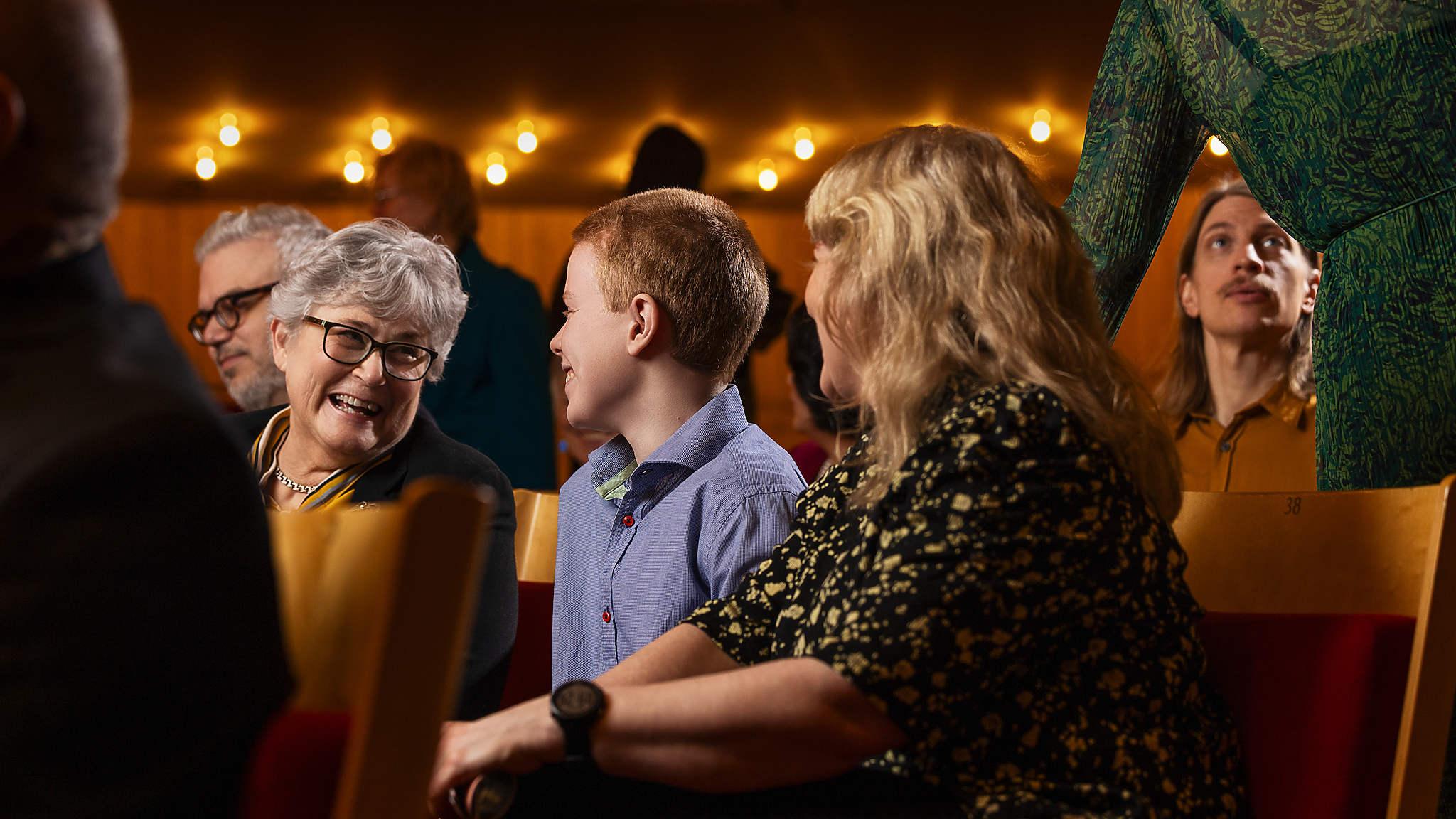 Publik i olika generationer sitter i konsertsalen och pratar med varandra före eller efter en konsert.