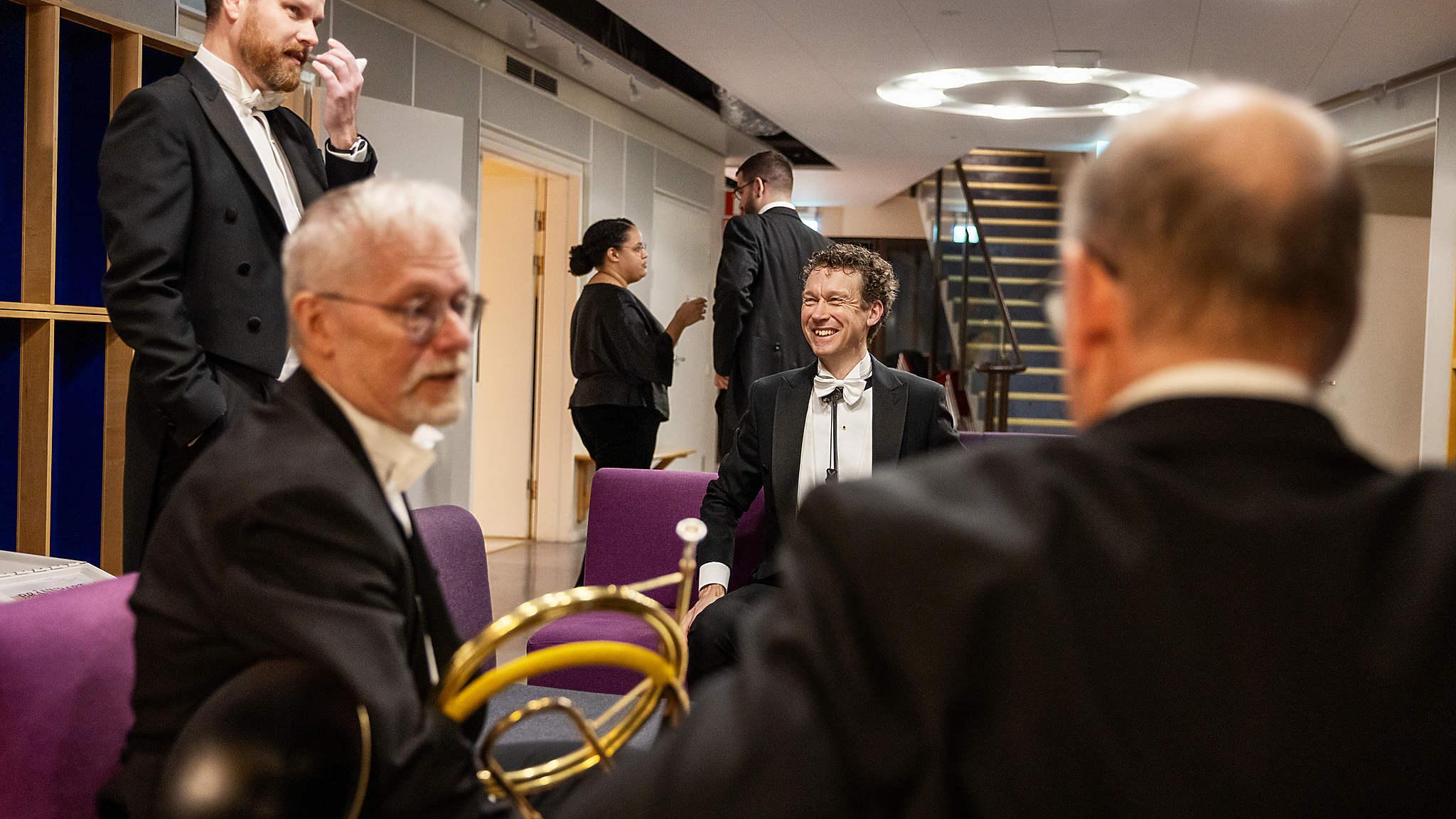 Några musiker skrattar och samtalar bakom scenen