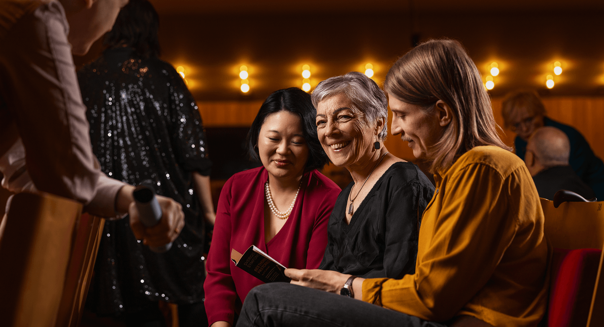 Publik i Berwaldhallen som ler och läser programbladet.