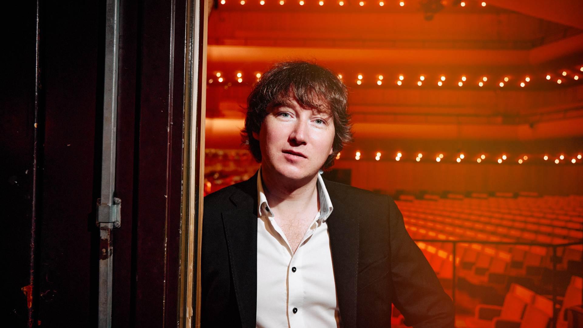 Maxim Emelyanychev i en dörröppning. I bakgrunden syns Berwaldhallens salong.