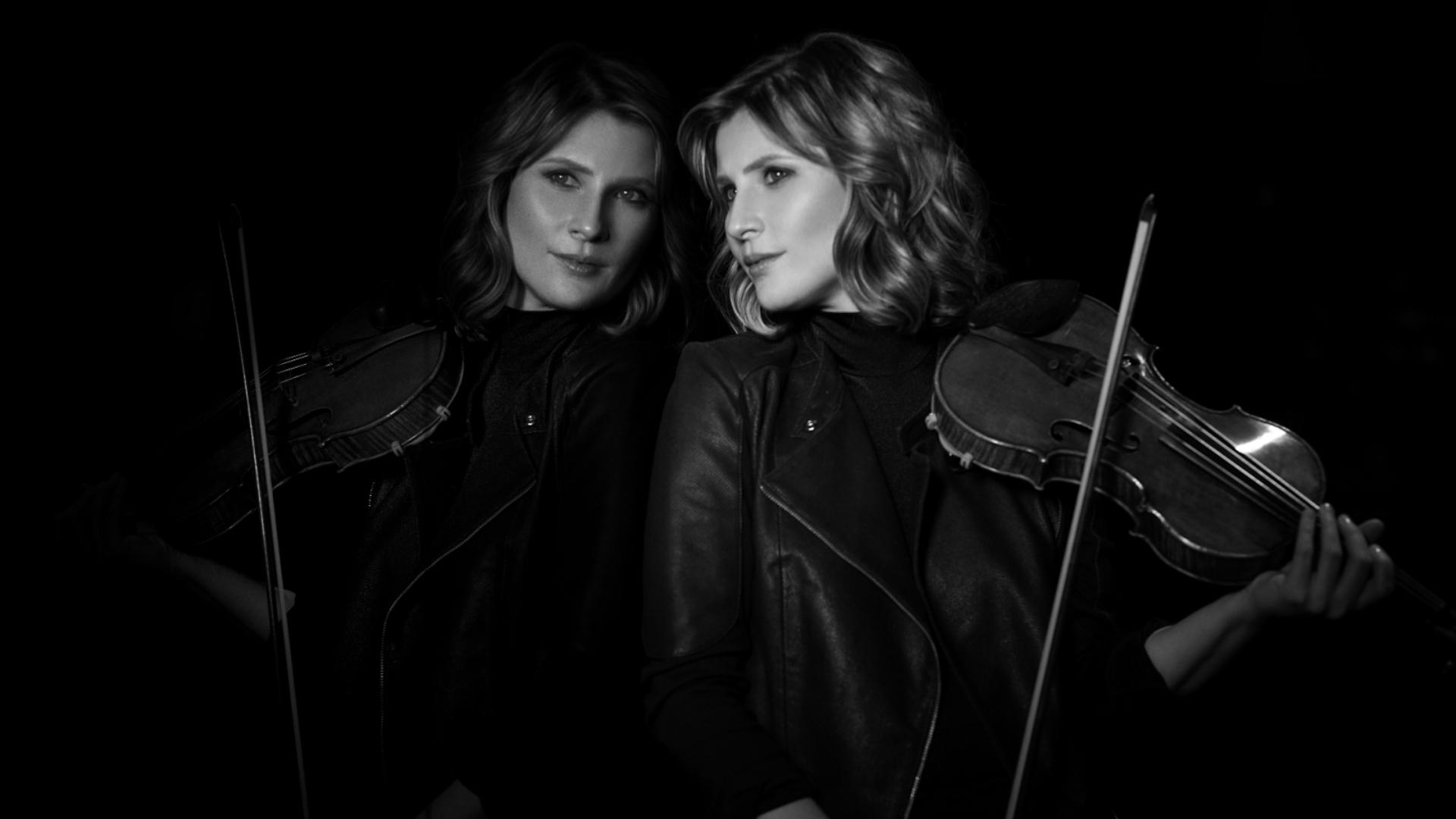 En svartvit bild där Lisa Bathiashvili står lutad mot en spegelvägg och håller i sin violin.