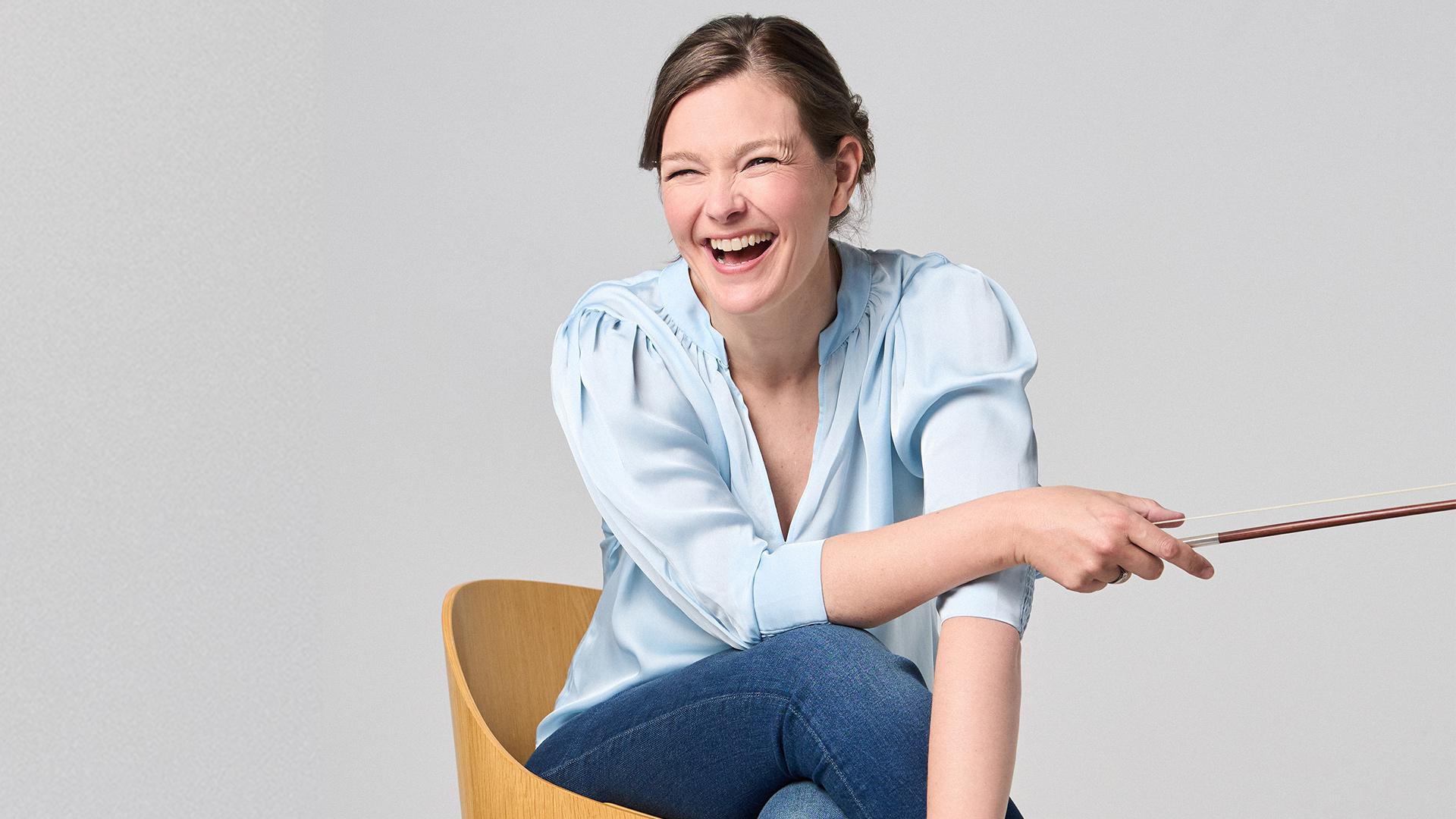 Janine Jansen, violinist, sitter och skrattar med en stråke i handen.