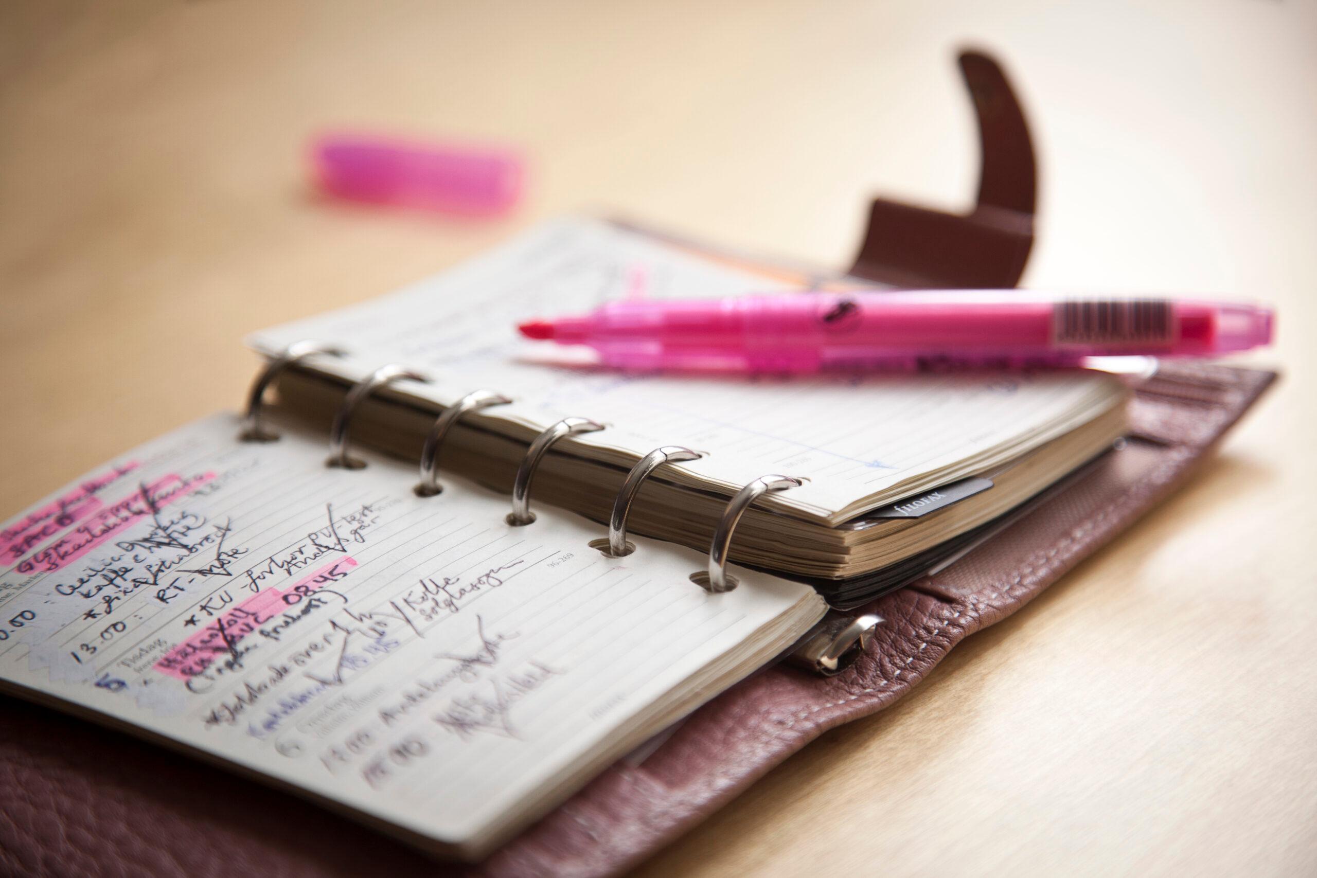 En almanacka ligger öppen och en rosa markeringspenna ovanpå.