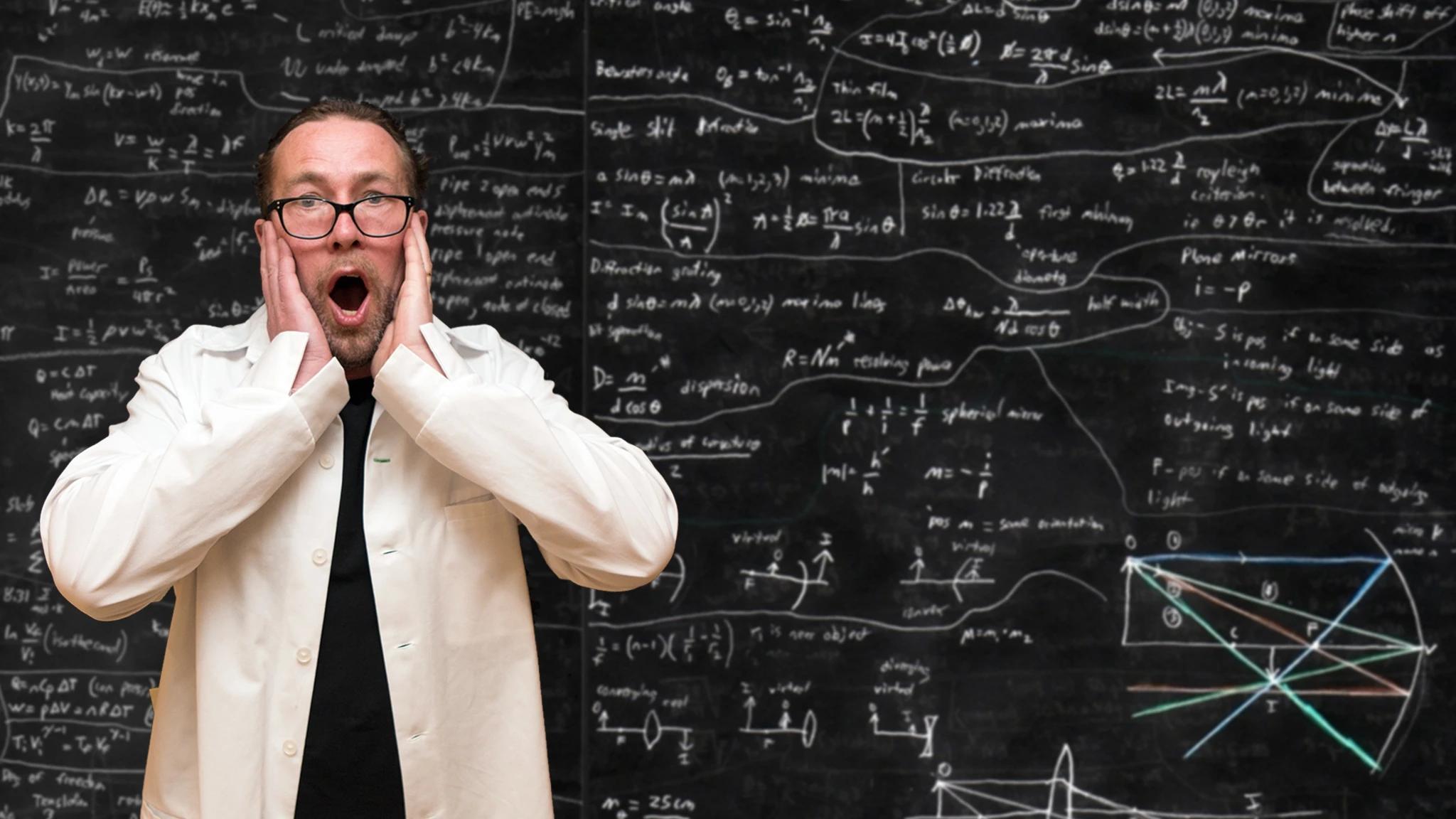 Man står i vit labbrock och håller händerna för ansiktet med munnen öppen i överväldigad gest. Bakom honom en svart tavla full av matematiska uträkningar.